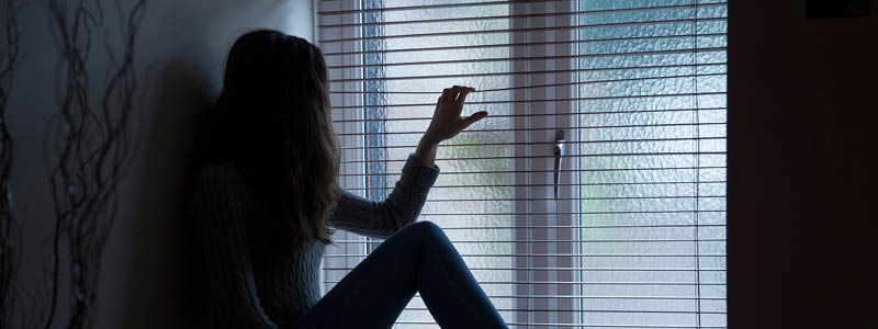 A silhouetted girl sitting in a dark room looking through a window