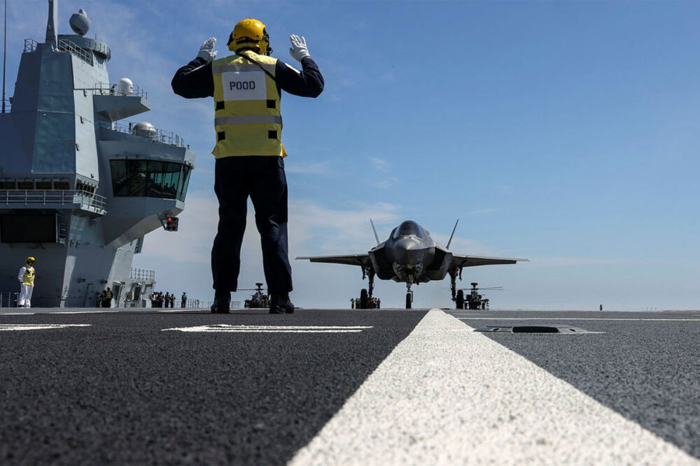 Ground crew on aircraft carrier with fighter jet