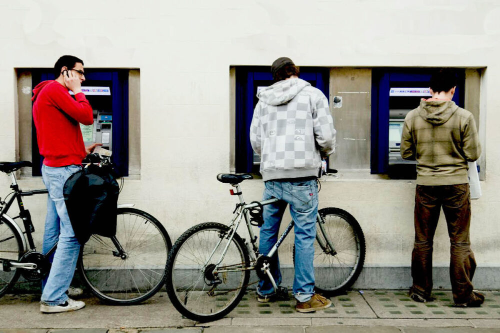 Three young men using a row of cashpoints