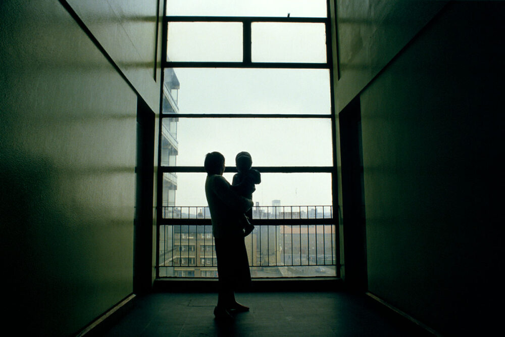 A woman holding a young child at the lifts of a block of flats