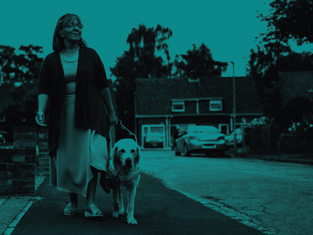 A woman walks with a guide dog, with a teal overlay.