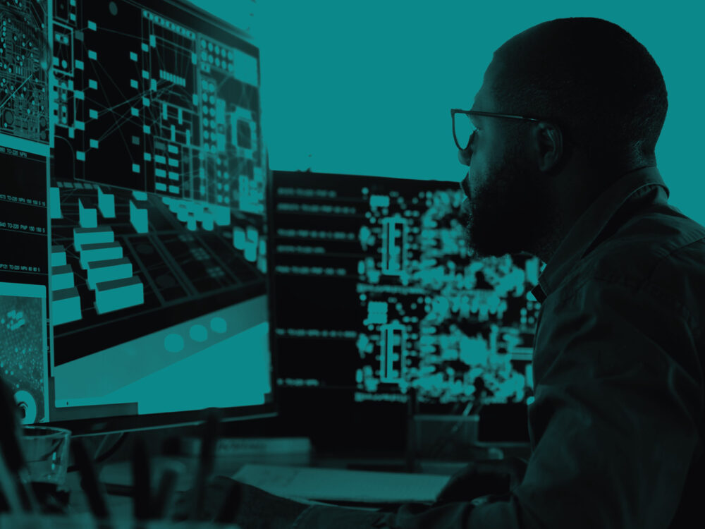 A man looks at a computer screen. The image has a cyan tint.