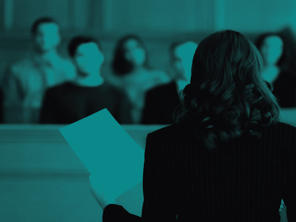 Image of a lawyer talking to a jury while holding a piece of paper, with a teal tint.
