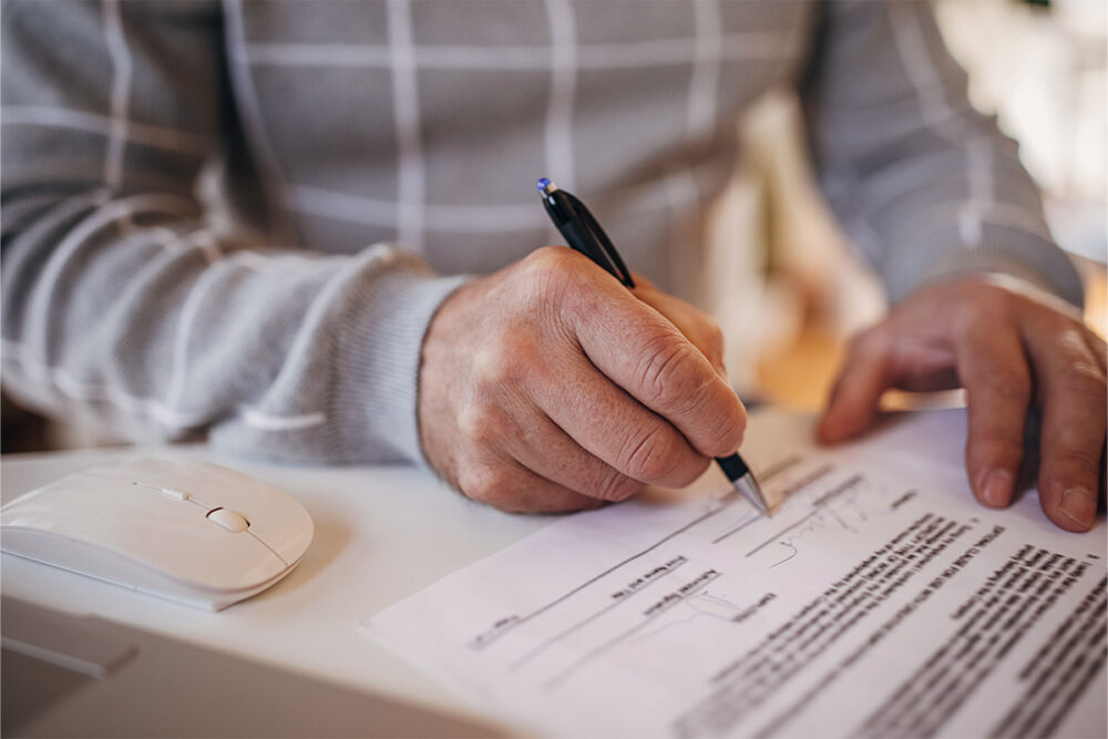 A person holding a pen signs their signature on an official-looking form